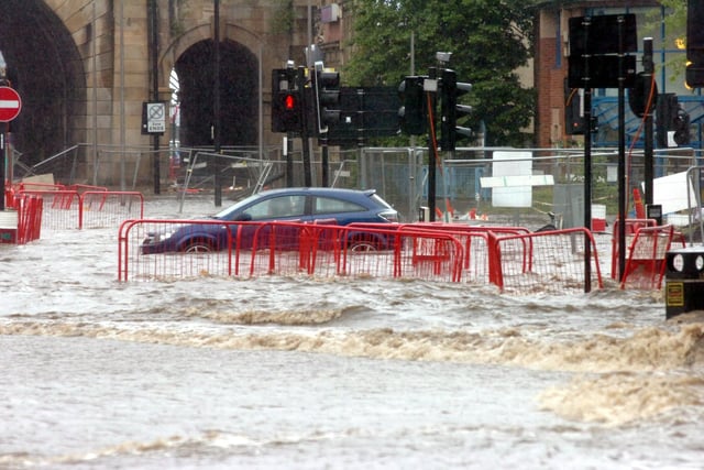 An urban road junction covered in floodwater. A car is partially submerged.