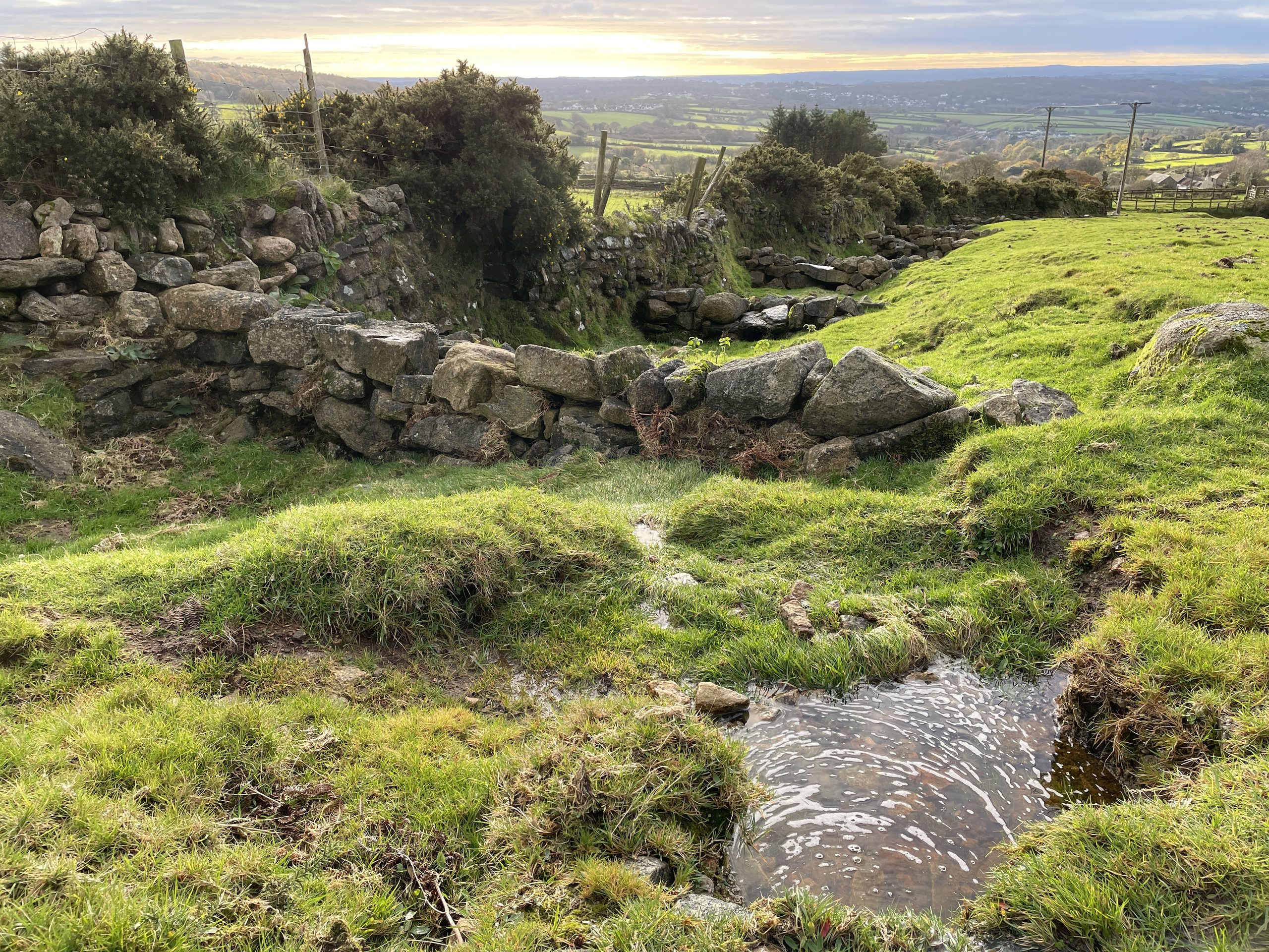 A leaky dam made from stone in a rural landscape.